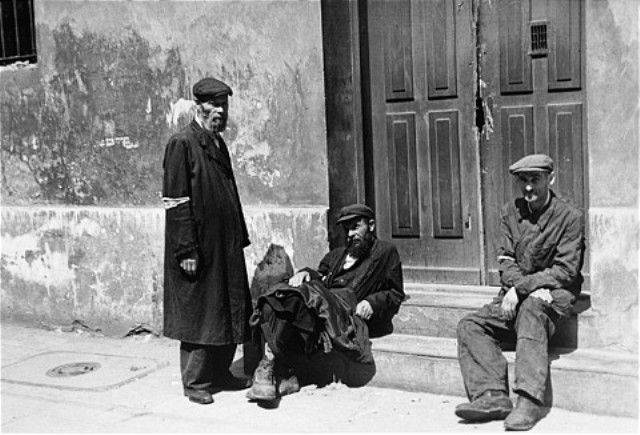 Three Jewish men sit outside the entrance to a building in the Warsaw ghetto